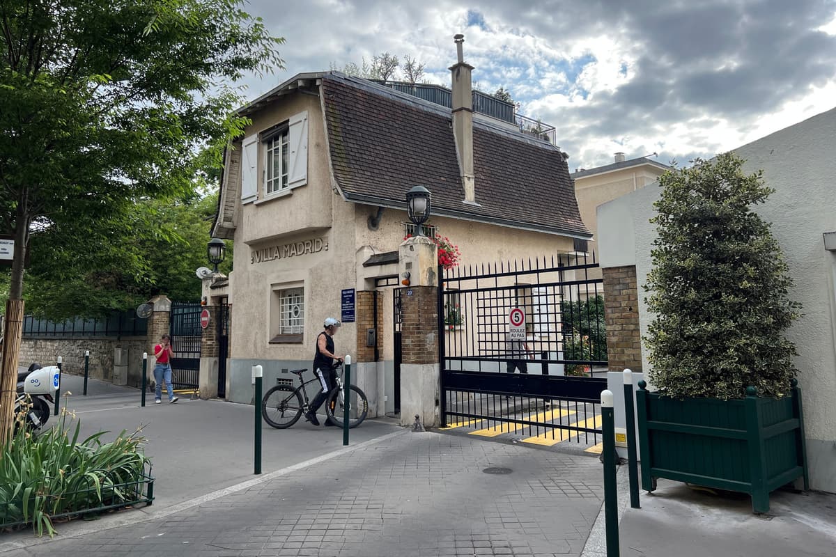 Pavillon d'entrée d'une voie privée : petite maison à toit d'ardoise et lucarne, près d'une grille ouverte.